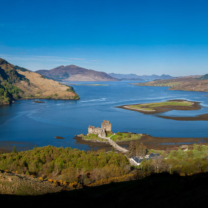 Blick von oben auf Eilean Donan Castle am Loch Alsh. Sonne auf Castle, Schatten im Vordergrund. Isle of Skye im Hintergrund, tiefblauer Himmel ohne Wolken oben