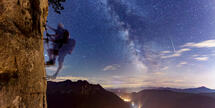 Hartmut Pönitz klettert nachts am Fels "Knieschladerer" auf Klettersteig "Schuastagangl". Sternenhimmel mit Spiralarm der Milchstrasse im Hintergrund.