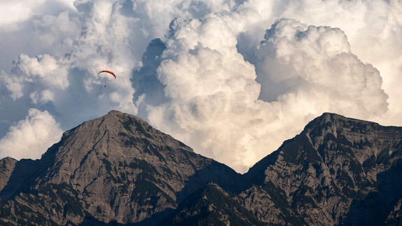 Gleitschirmflieger "flieht" vor Wolkenformation wie von einer Explosion. Unter den Wolken und unter dem Paraglider steht das Sonntagshorn bei Ruhpolding.