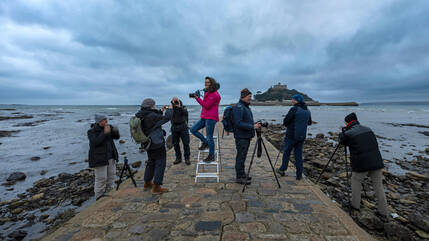 Fotogruppe steht auf Kopsteinpflasterweg vor St. Michael´s Mount in Cornwall. Eine Fotografin, in der Mitte, etwas höher auf der Leiter.